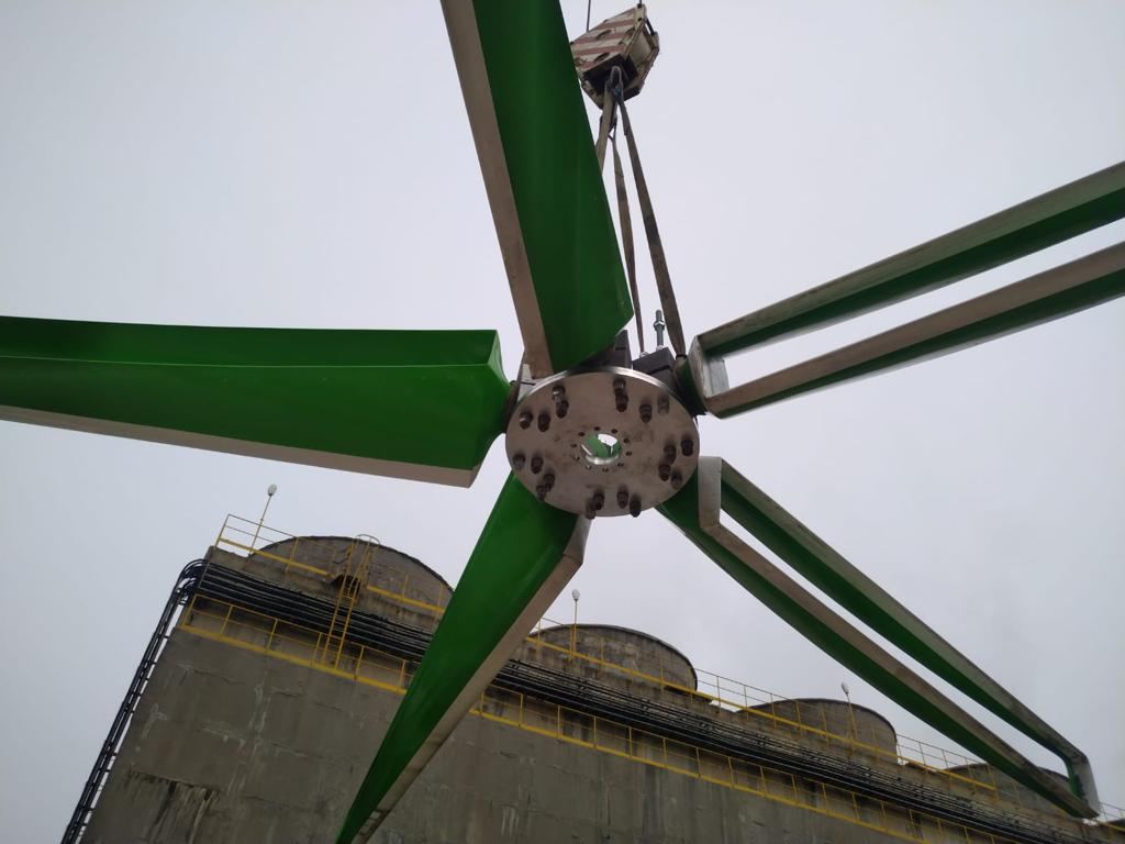 GT Green Fan on a crane hook above a concrete cooling tower at a power plant